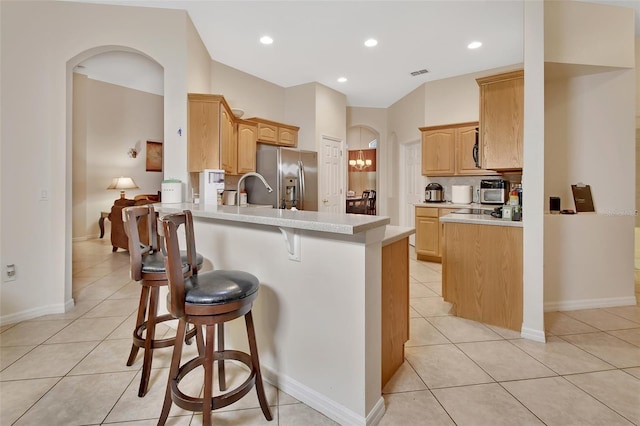 kitchen featuring sink, stainless steel fridge, light tile patterned floors, a kitchen bar, and kitchen peninsula