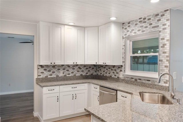 kitchen featuring white cabinetry, sink, light stone countertops, stainless steel dishwasher, and backsplash