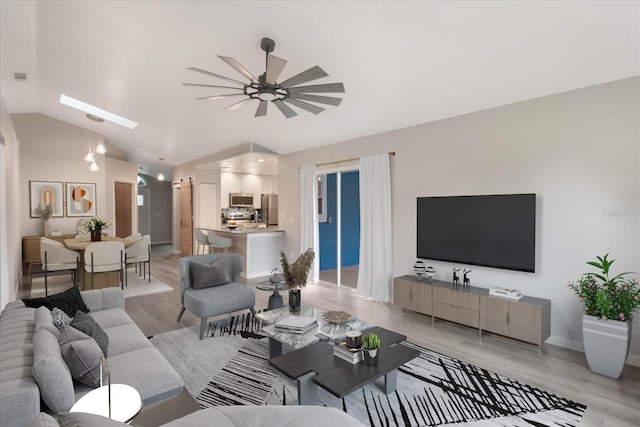 living room featuring light wood finished floors, lofted ceiling with skylight, a ceiling fan, and baseboards