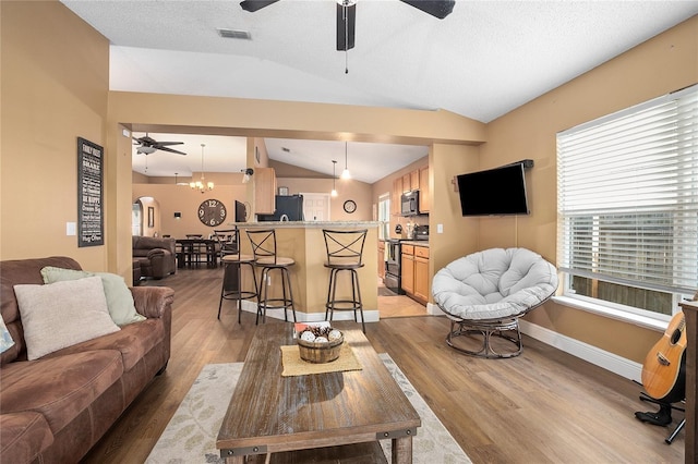 living room with a chandelier, a textured ceiling, light wood-type flooring, and lofted ceiling