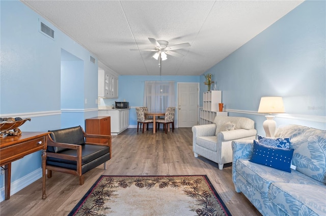 living room featuring ceiling fan, a textured ceiling, and light wood-type flooring