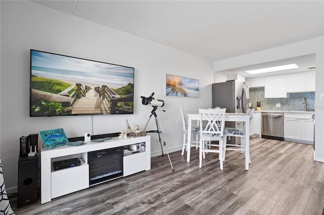 kitchen with decorative backsplash, appliances with stainless steel finishes, sink, white cabinets, and light hardwood / wood-style floors