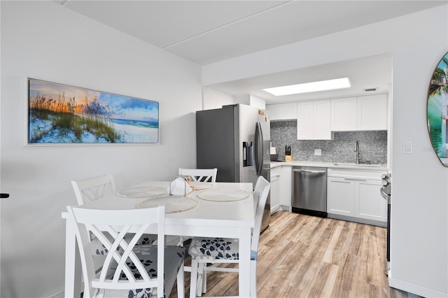 kitchen featuring backsplash, sink, light wood-type flooring, appliances with stainless steel finishes, and white cabinetry