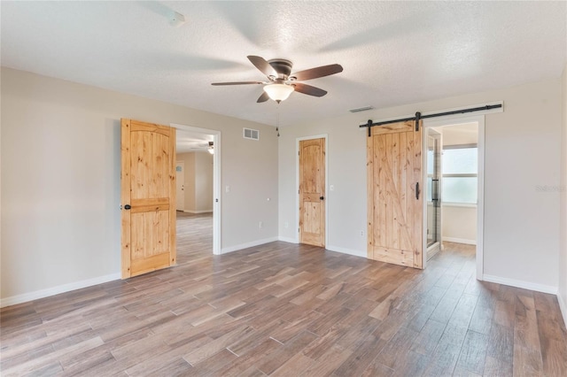 spare room featuring hardwood / wood-style floors, ceiling fan, a barn door, and a textured ceiling