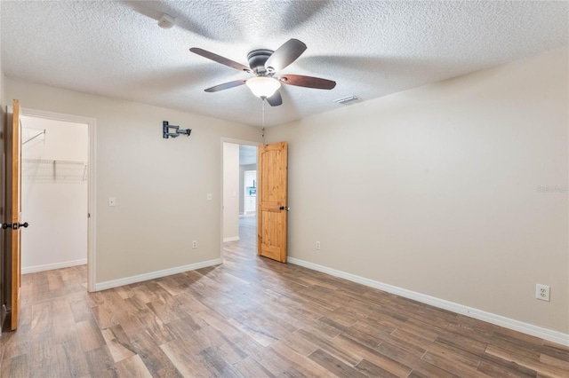 unfurnished bedroom featuring wood-type flooring, a closet, a spacious closet, and ceiling fan