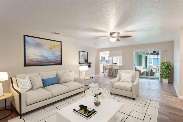 living area with a ceiling fan, visible vents, a textured ceiling, and light wood finished floors