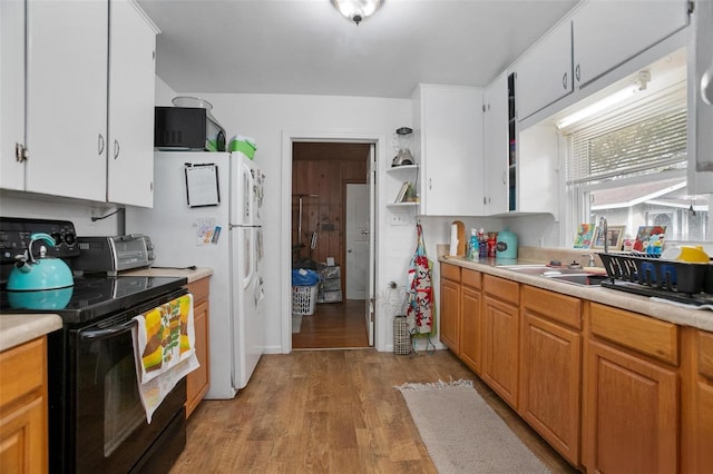 kitchen featuring black range with electric stovetop, sink, white cabinets, and light hardwood / wood-style floors