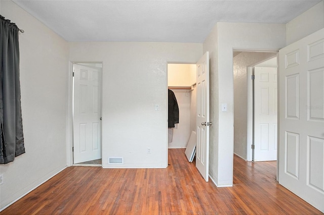 unfurnished bedroom with a walk in closet, a closet, and hardwood / wood-style flooring