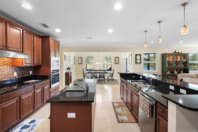 kitchen featuring decorative light fixtures, sink, appliances with stainless steel finishes, and an island with sink