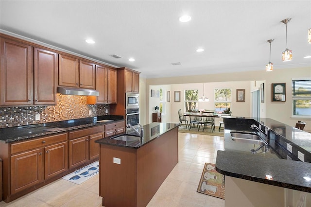 kitchen featuring dark stone counters, sink, appliances with stainless steel finishes, and an island with sink