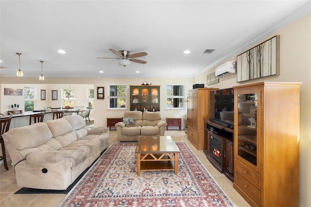 living room with ceiling fan, a wall mounted air conditioner, crown molding, a tiled fireplace, and light tile patterned flooring