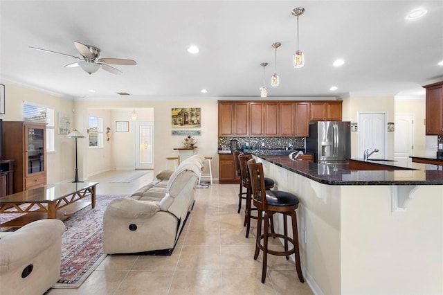 kitchen with stainless steel fridge, an island with sink, dark stone counters, pendant lighting, and a breakfast bar