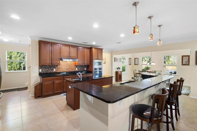 kitchen featuring pendant lighting, sink, stainless steel appliances, decorative backsplash, and a large island with sink