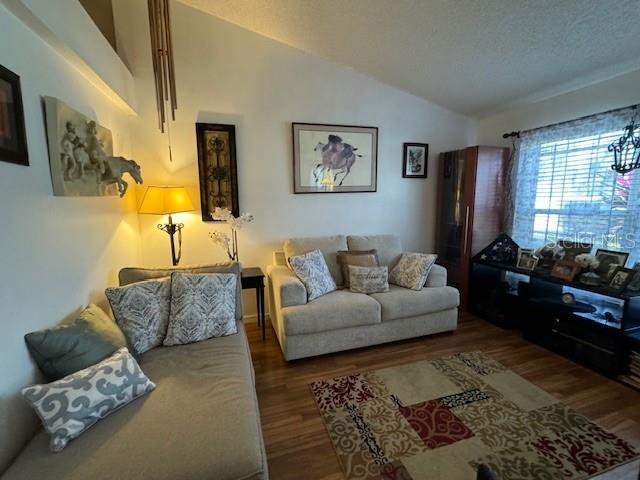 living room featuring wood-type flooring, a textured ceiling, and vaulted ceiling