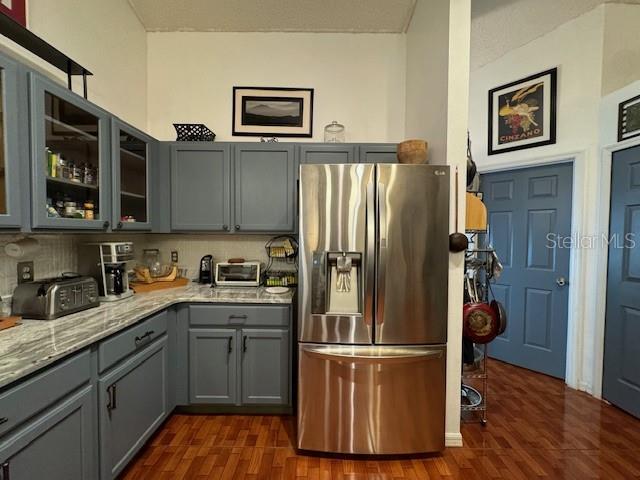 kitchen with stainless steel refrigerator with ice dispenser, gray cabinets, light stone counters, tasteful backsplash, and dark hardwood / wood-style flooring