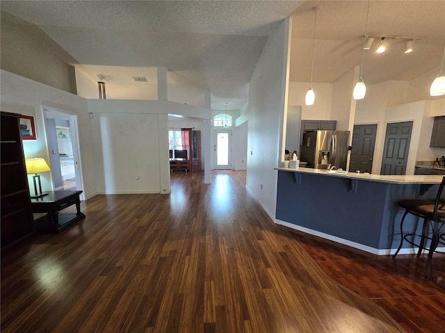 kitchen featuring a breakfast bar, high vaulted ceiling, hanging light fixtures, stainless steel refrigerator with ice dispenser, and kitchen peninsula