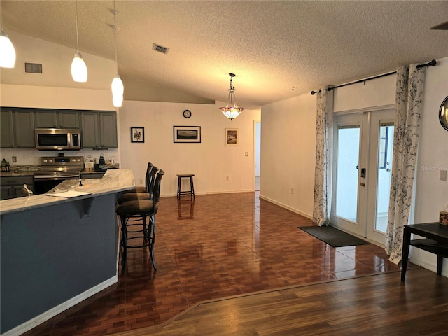 kitchen featuring appliances with stainless steel finishes, a breakfast bar, a textured ceiling, pendant lighting, and lofted ceiling