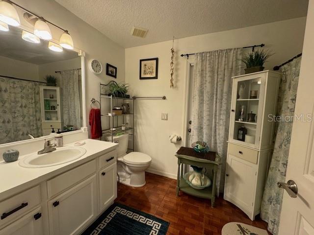 bathroom with parquet flooring, vanity, a textured ceiling, and toilet