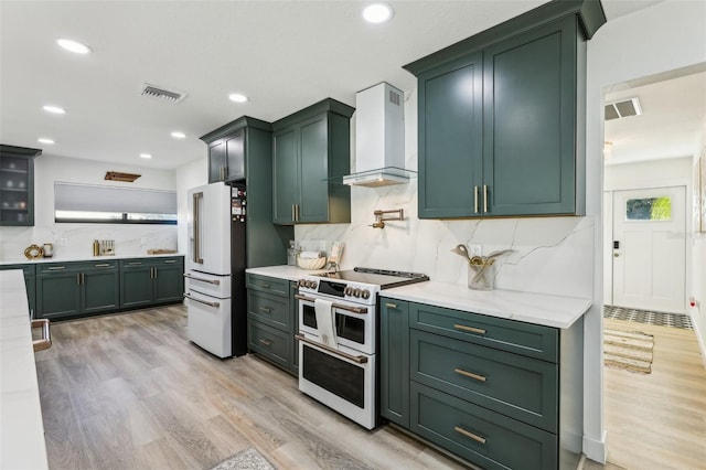 kitchen with double oven range, backsplash, wall chimney range hood, light hardwood / wood-style floors, and high end fridge