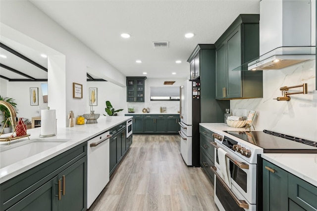 kitchen featuring sink, wall chimney exhaust hood, green cabinets, light hardwood / wood-style flooring, and white appliances