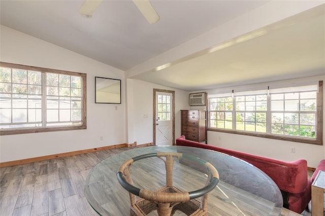 living area with a wall unit AC, a wealth of natural light, light hardwood / wood-style floors, and vaulted ceiling