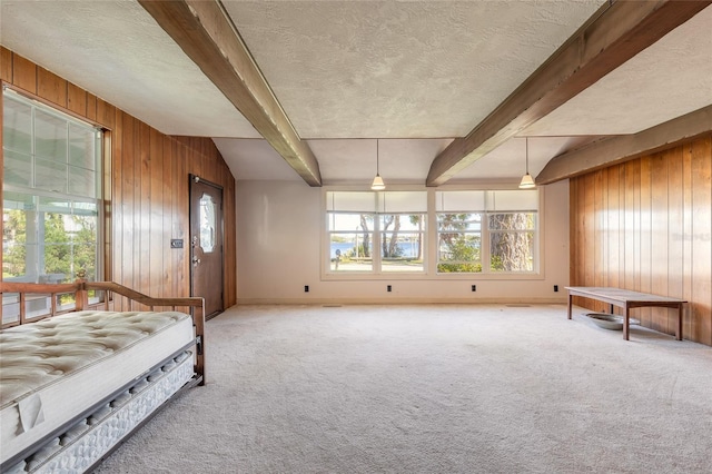 carpeted bedroom with beam ceiling, a textured ceiling, and wooden walls