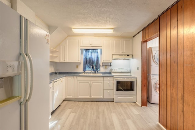 kitchen with white cabinets, sink, white appliances, and stacked washer and dryer