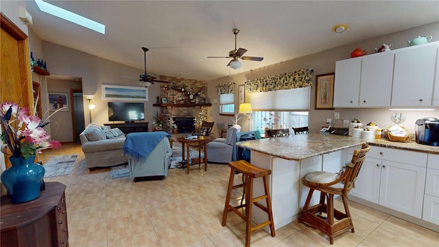 kitchen with a breakfast bar, lofted ceiling with skylight, ceiling fan, a large fireplace, and white cabinetry