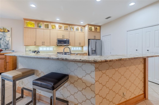 kitchen featuring light brown cabinetry, light stone countertops, a kitchen breakfast bar, and stainless steel appliances