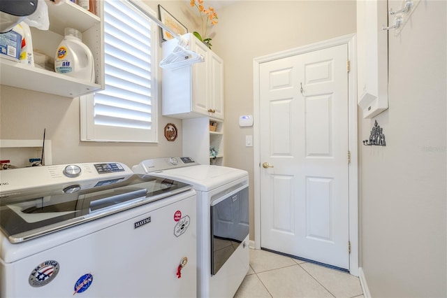 laundry room featuring washer and clothes dryer, light tile patterned floors, a healthy amount of sunlight, and cabinets