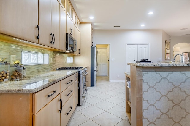 kitchen with appliances with stainless steel finishes, light brown cabinetry, backsplash, light stone counters, and light tile patterned floors