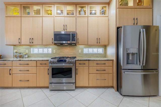 kitchen with light brown cabinets, light tile patterned floors, light stone counters, and stainless steel appliances