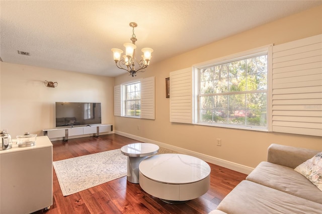 living room featuring a textured ceiling, dark wood-type flooring, a healthy amount of sunlight, and a chandelier