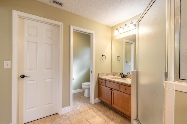 bathroom featuring a textured ceiling, tile patterned flooring, toilet, walk in shower, and vanity