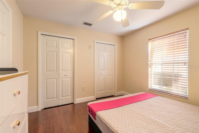 bedroom featuring ceiling fan, dark hardwood / wood-style floors, and multiple closets