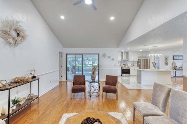 living room with ceiling fan, light hardwood / wood-style flooring, high vaulted ceiling, and a textured ceiling