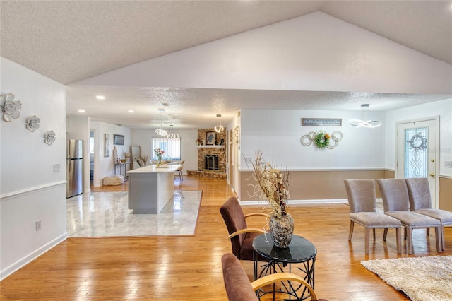 living room with light hardwood / wood-style floors, lofted ceiling, a textured ceiling, and a brick fireplace