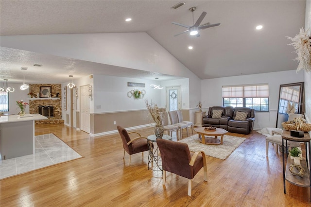 living room featuring light wood-type flooring, a brick fireplace, a textured ceiling, ceiling fan, and high vaulted ceiling