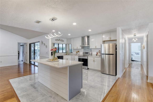 kitchen featuring white cabinetry, stainless steel appliances, wall chimney range hood, tasteful backsplash, and pendant lighting