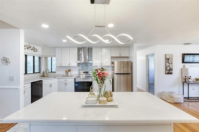 kitchen featuring sink, wall chimney range hood, pendant lighting, a textured ceiling, and appliances with stainless steel finishes