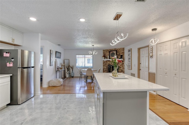 kitchen with stainless steel fridge, a fireplace, decorative light fixtures, white cabinets, and a center island