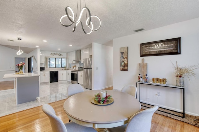 dining area with a chandelier, a textured ceiling, light hardwood / wood-style floors, and sink