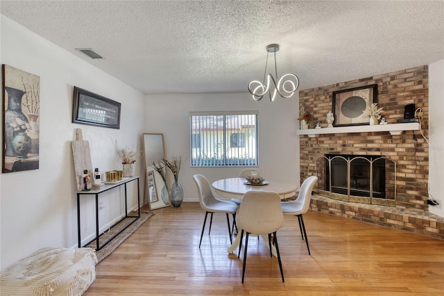 dining room featuring a notable chandelier, wood-type flooring, a textured ceiling, and a brick fireplace