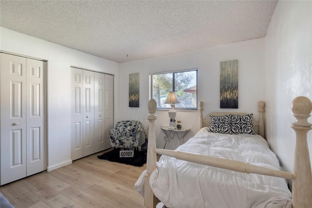 bedroom with light wood-type flooring, a textured ceiling, and multiple closets