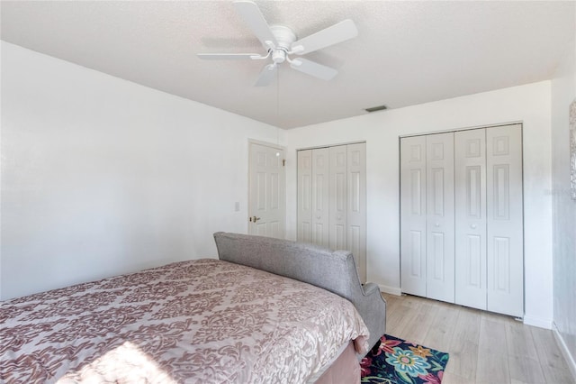 bedroom featuring a textured ceiling, two closets, light hardwood / wood-style flooring, and ceiling fan