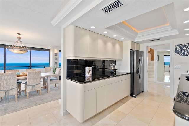 kitchen featuring a water view, stainless steel refrigerator with ice dispenser, hanging light fixtures, ornamental molding, and a tray ceiling