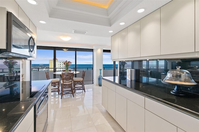 kitchen featuring decorative backsplash, a raised ceiling, crown molding, light tile patterned floors, and a water view