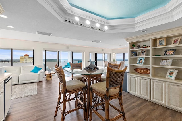 dining area with hardwood / wood-style flooring, a water view, crown molding, and a tray ceiling