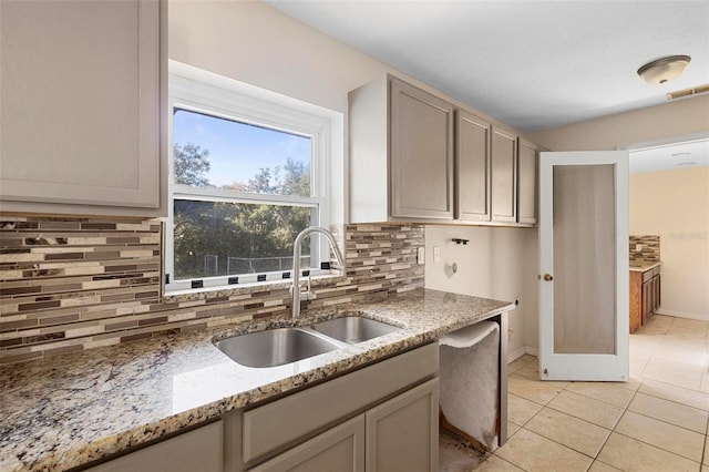 kitchen featuring sink, light tile patterned floors, backsplash, light stone countertops, and gray cabinetry