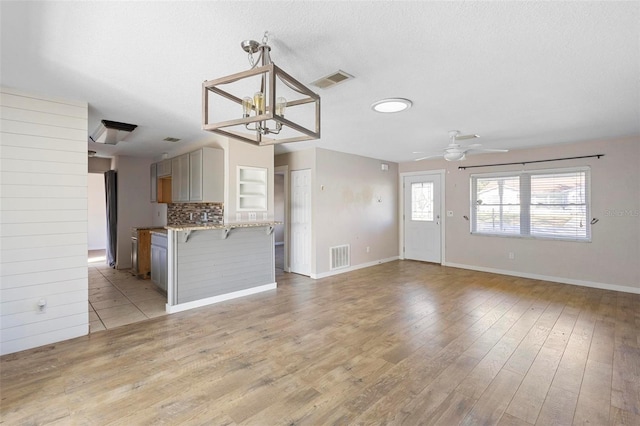 kitchen featuring hanging light fixtures, light hardwood / wood-style floors, backsplash, ceiling fan with notable chandelier, and a kitchen breakfast bar